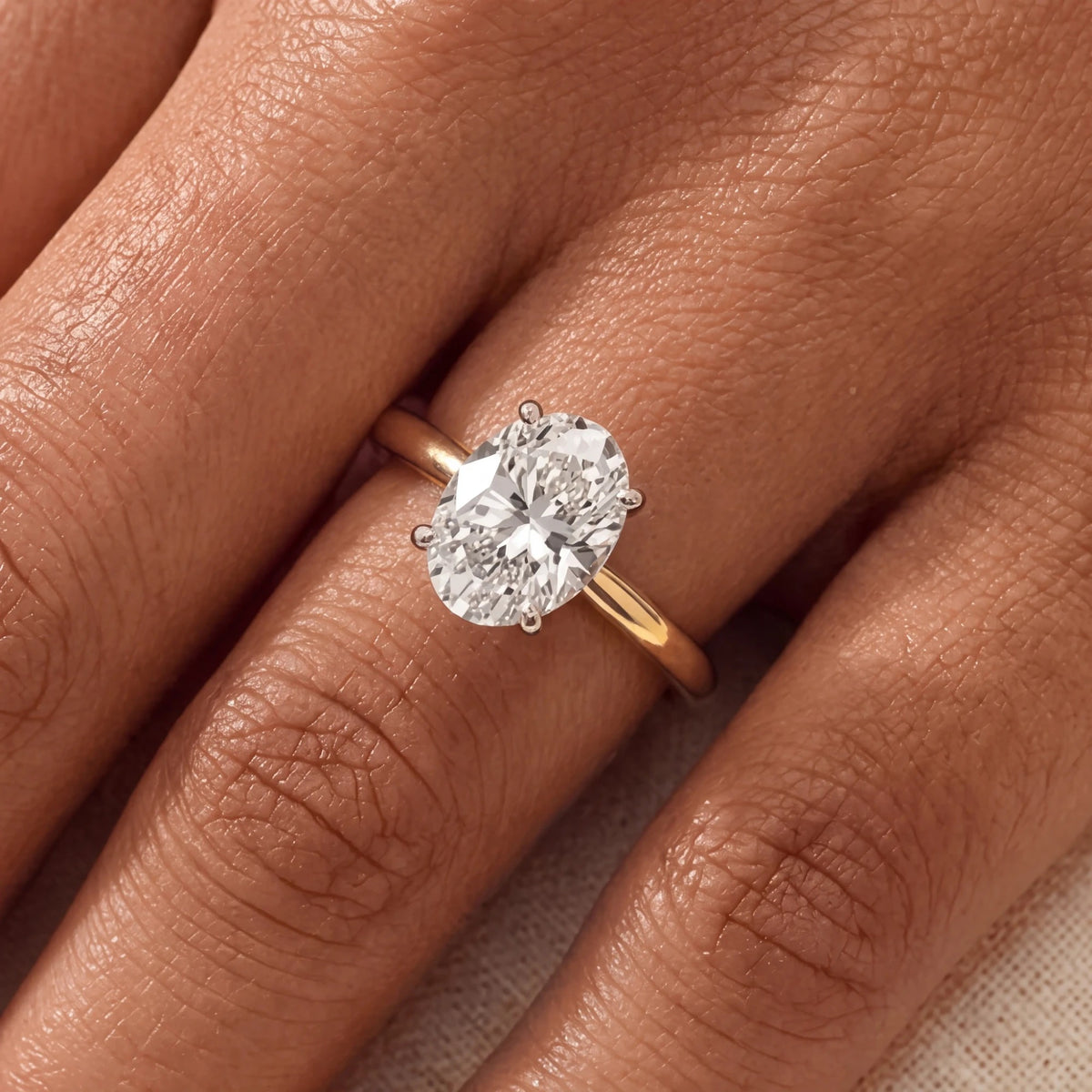 Close-up van de ovale solitaire verlovingsring 2.0 ct in 14k geelgoud aan de hand, op ware grootte (steen 10,5 mm)