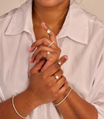 Een gestyled modelbeeld dat veel 14k gouden sieraden draagt waaronder solitaire ringen met 1.0, 1.5 en 2.0ct diamanten. Daarbij armbanden en eeuwigheid ring