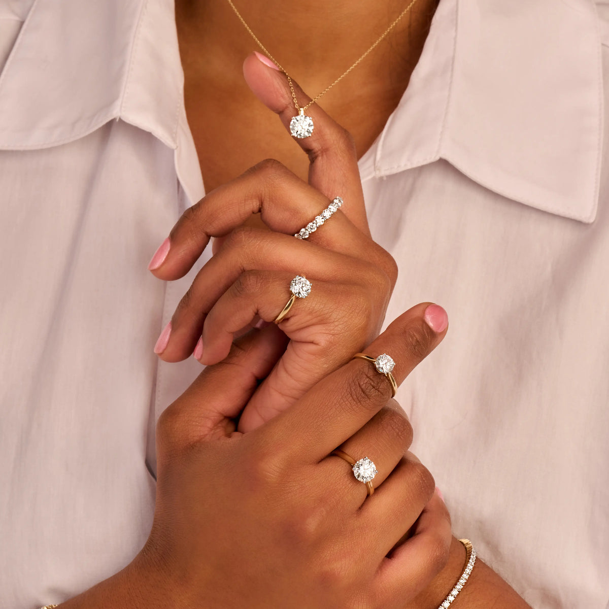 Een gestyled modelbeeld dat veel 14k gouden sieraden draagt waaronder solitaire ringen met 1.0, 1.5 en 2.0ct diamanten. Daarbij armbanden en eeuwigheid ring