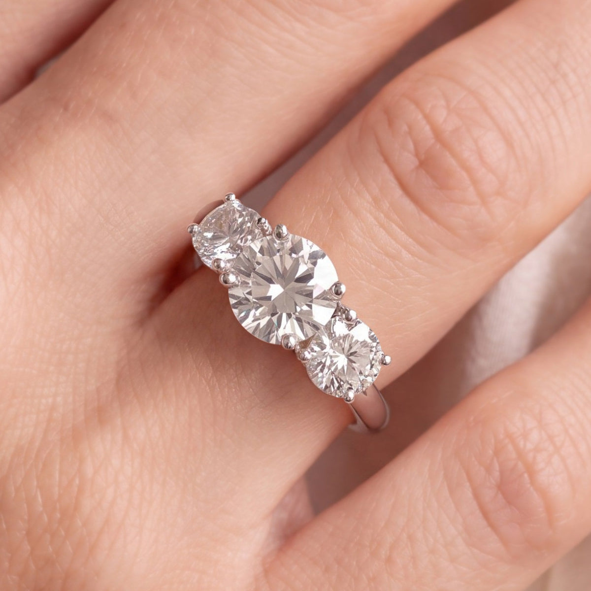 Ronde trilogie verlovingsring 2.5 ct in 14k witgoud aan de hand, op ware grootte (stenen 6,8 + 2× 5,5 mm)