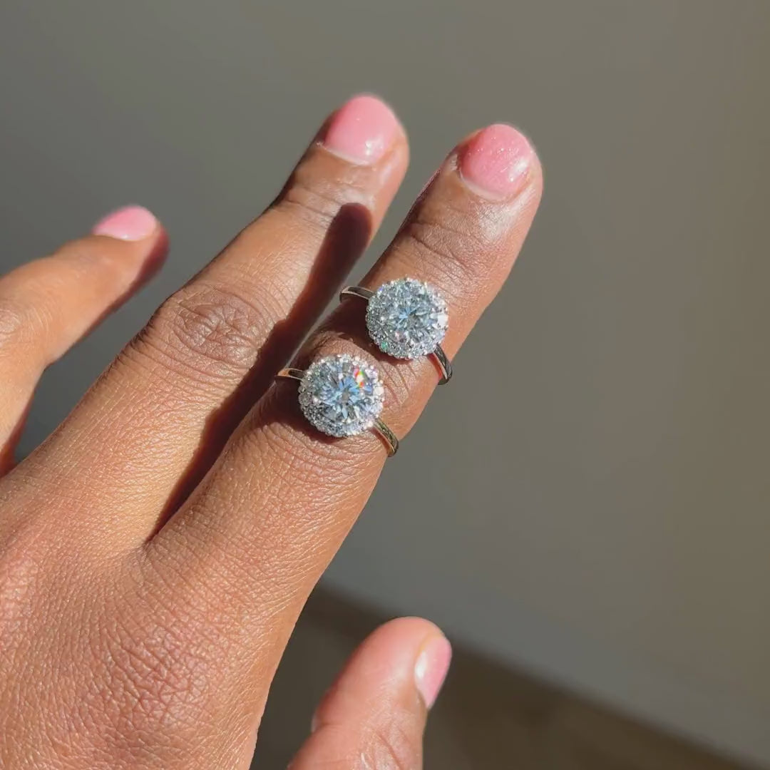 Ronde halo verlovingsring 1.75 ct in witgoud en geelgoud naast elkaar aan de hand